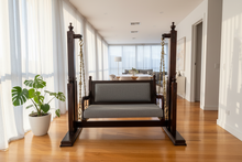 Load image into Gallery viewer, Wooden swing with gray cushion in a room with large windows and a plant.
